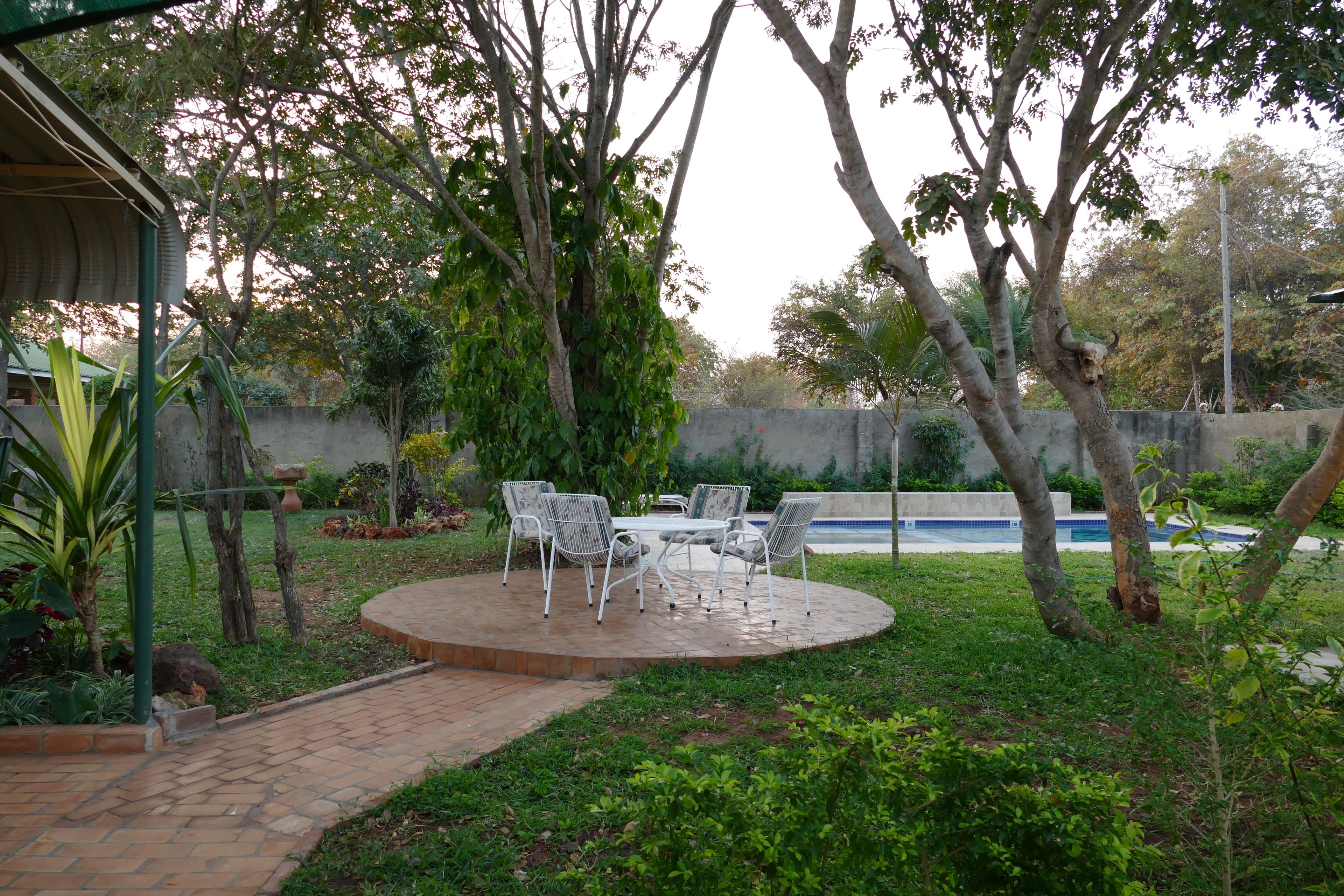 A patio area with a table and chairs, surrounded by greenery and a swimming pool.