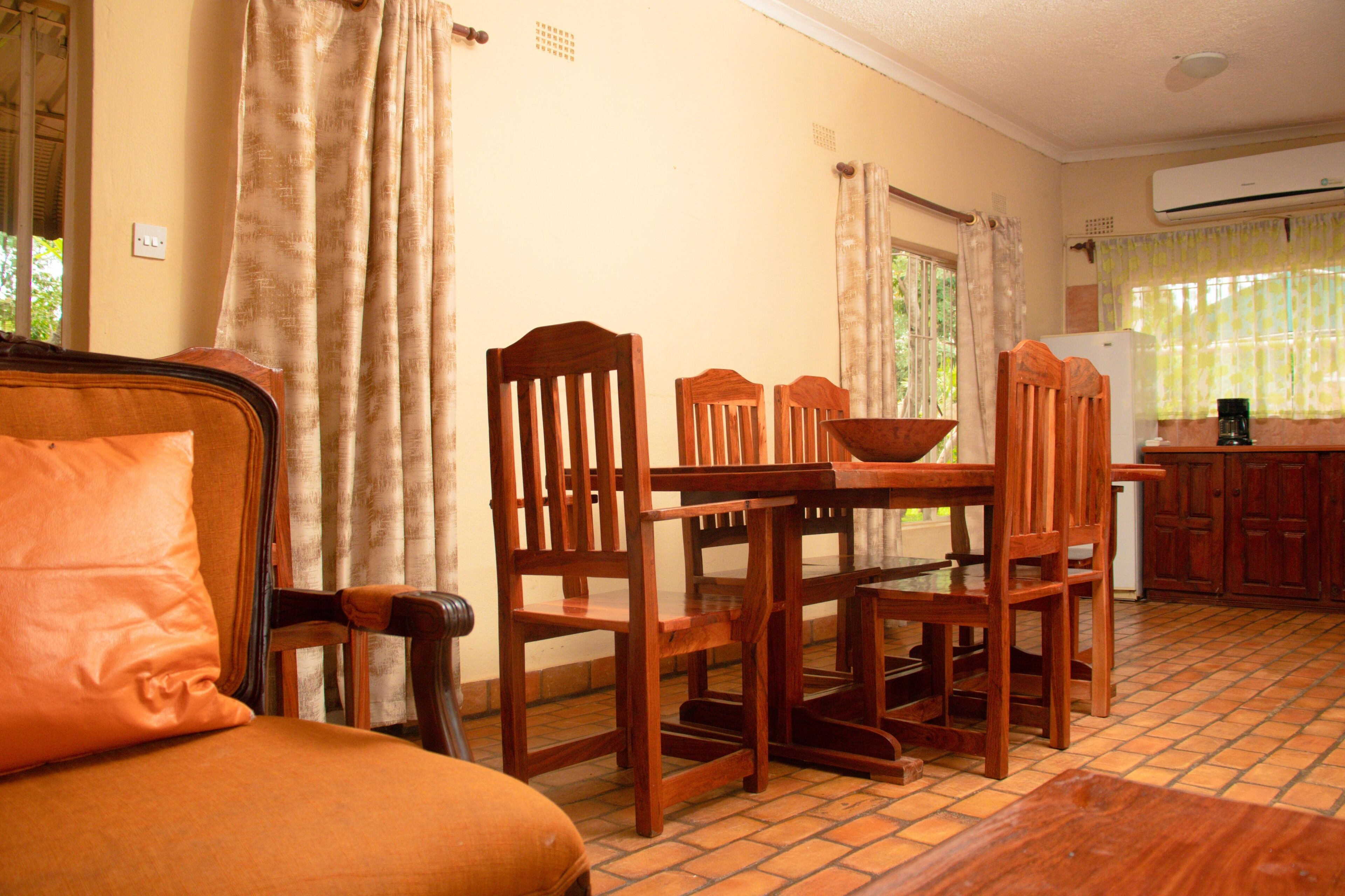 Un área de comedor con una mesa y sillas de madera, un sofá y una cocina al fondo.