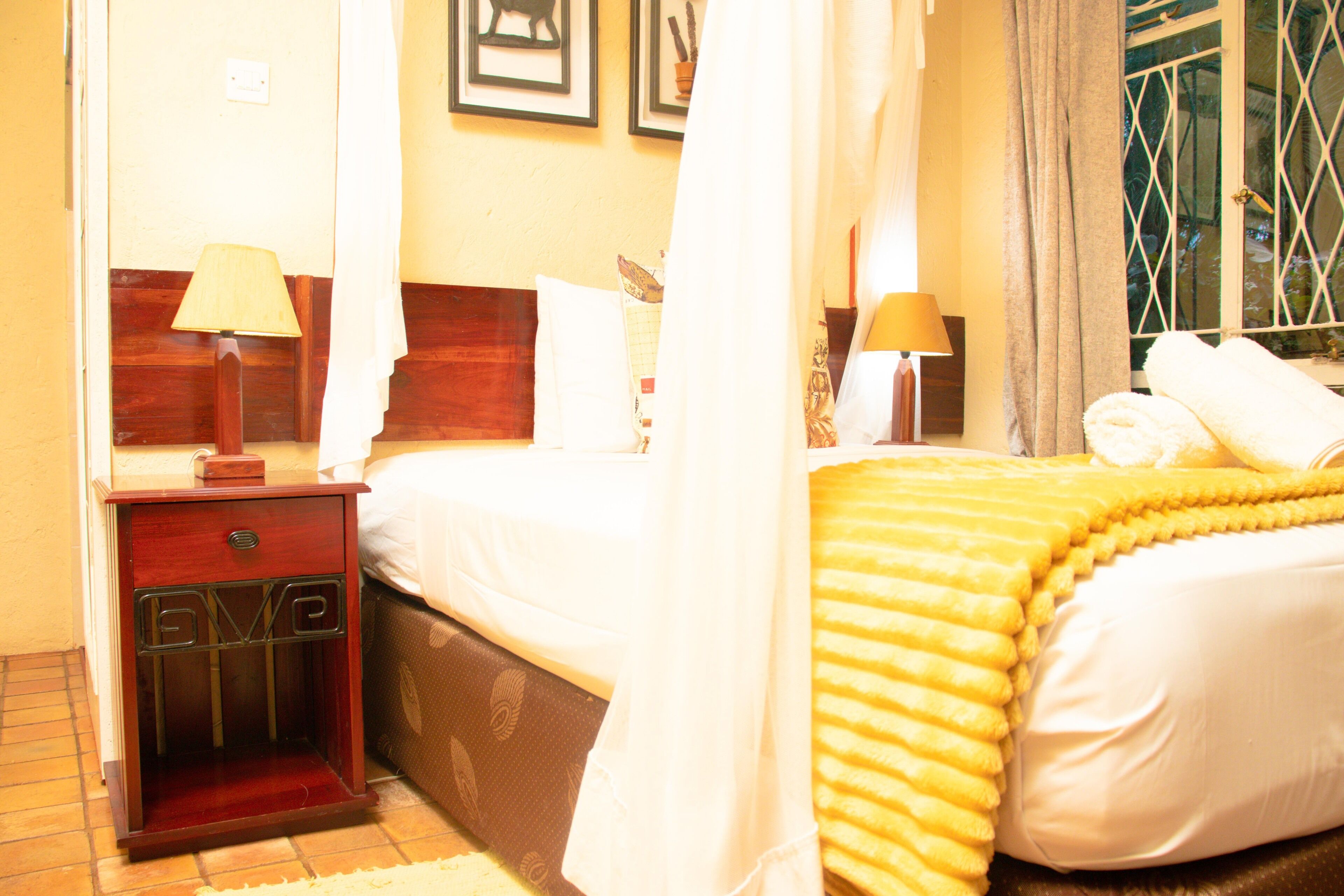 A hotel room with a bed, a nightstand, a lamp, and a window with curtains.