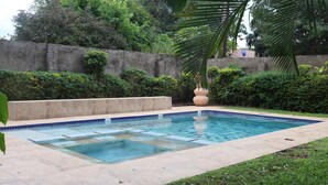 Ein rechteckiger Swimmingpool mit klarem, blauem Wasser, umgeben von einer gefliesten Terrasse und üppigem Grün.