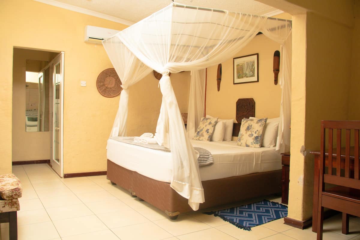 A bedroom with a four-poster bed, a wooden chair, and a blue patterned rug.