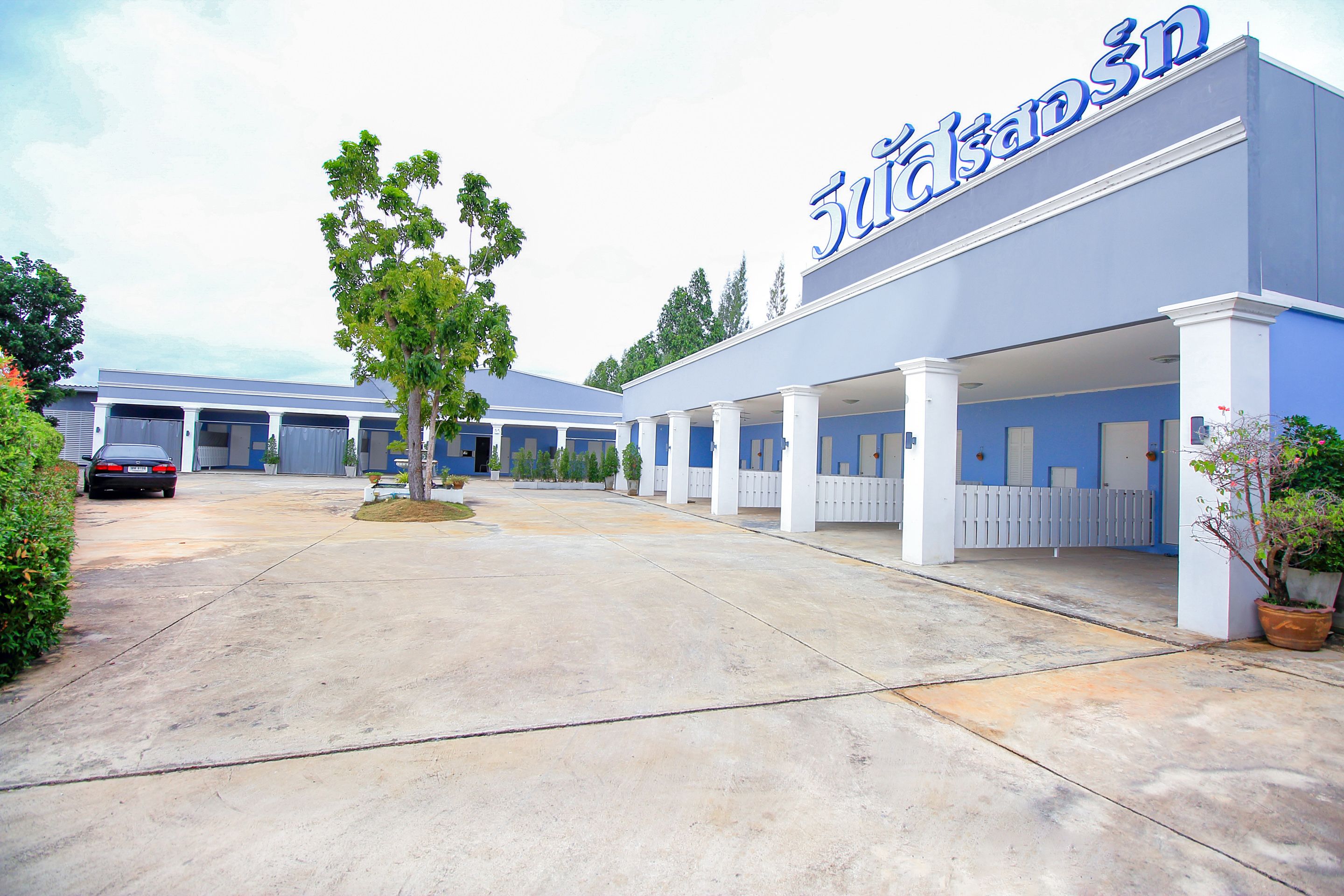 A hotel with a blue facade and white columns, featuring a covered outdoor area with a tree and potted plants.