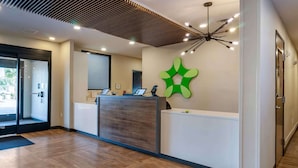 A reception area with a wooden reception desk, a green wall decoration, and a modern ceiling light fixture. - Extended Stay America Premier Suites Port Charlotte I75 (Port Charlotte)