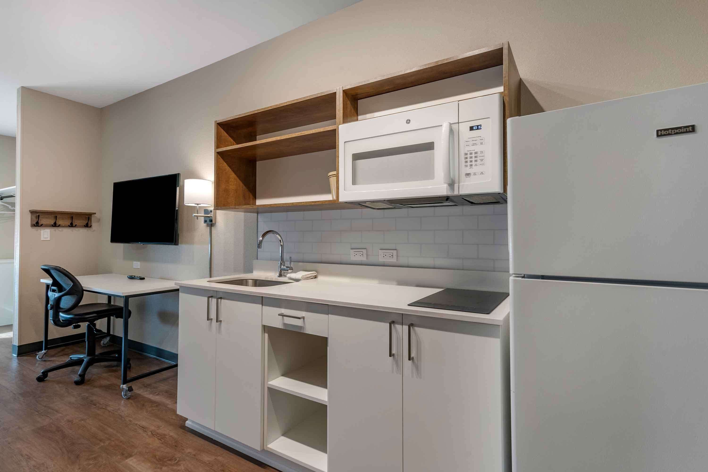 A compact kitchen with white cabinetry, a microwave, a refrigerator, and a small sink.