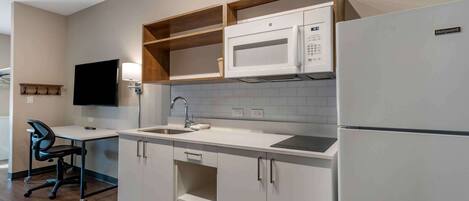 A compact kitchen with white cabinetry, a microwave, a refrigerator, and a small sink.