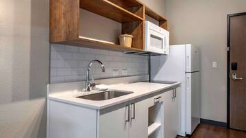 A compact kitchen with a white countertop, a double sink, a microwave, and a refrigerator.
