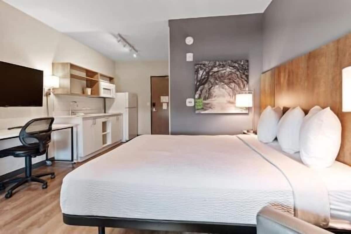 Ein Hotelzimmer mit Bett, Schreibtisch, Stuhl, einer Küchenzeile und einem Gemälde an der Wand.