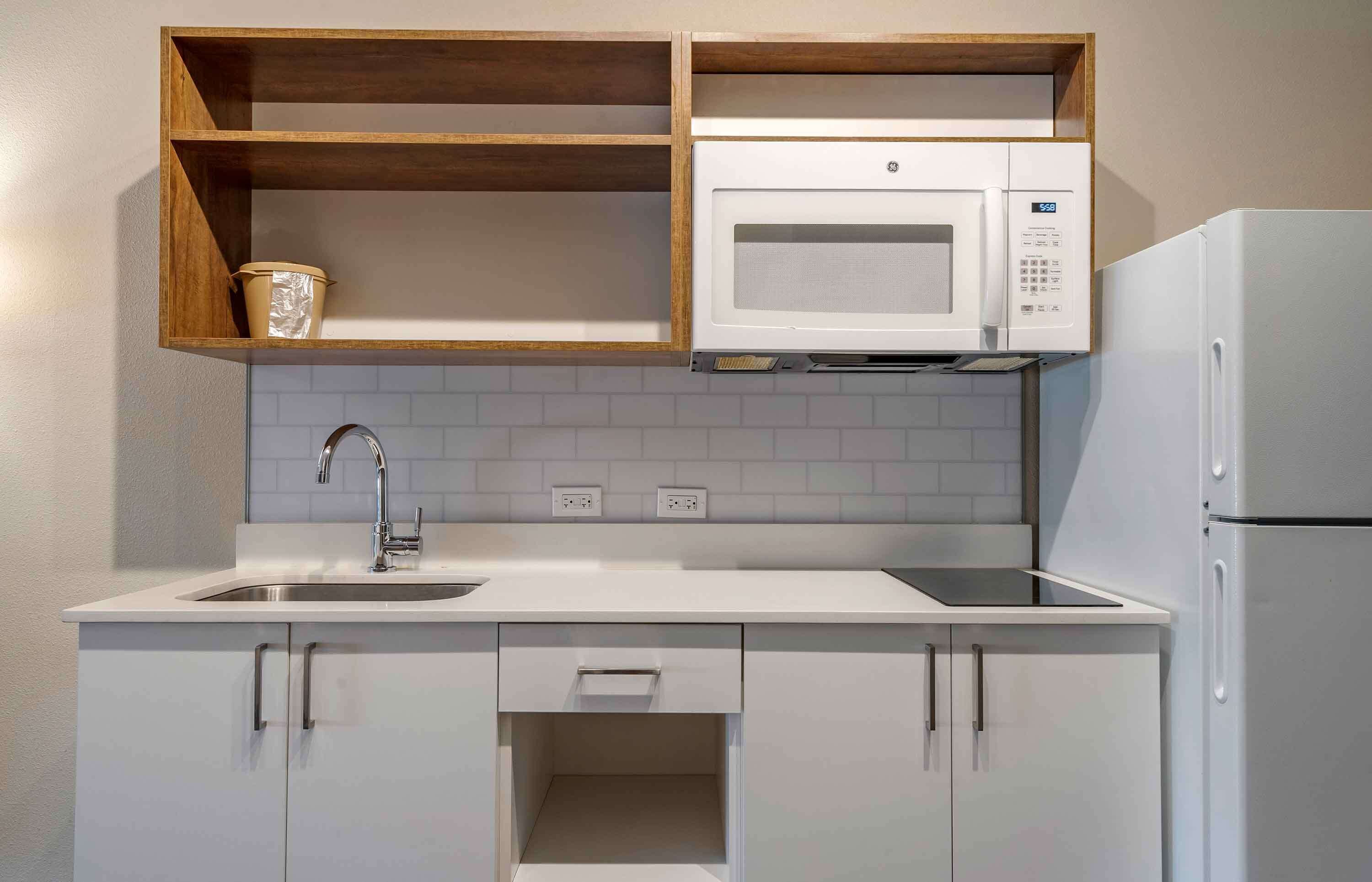 A compact kitchen with white cabinetry, a built-in microwave, and a refrigerator.