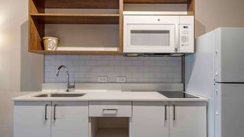 A compact kitchen with white cabinetry, a built-in microwave, and a refrigerator.