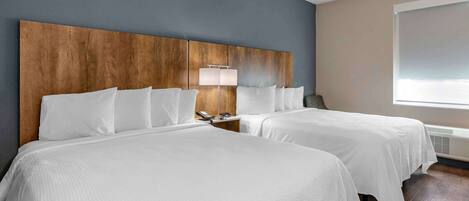 A hotel room with two beds, a wooden headboard, a bedside lamp, and a large window.
