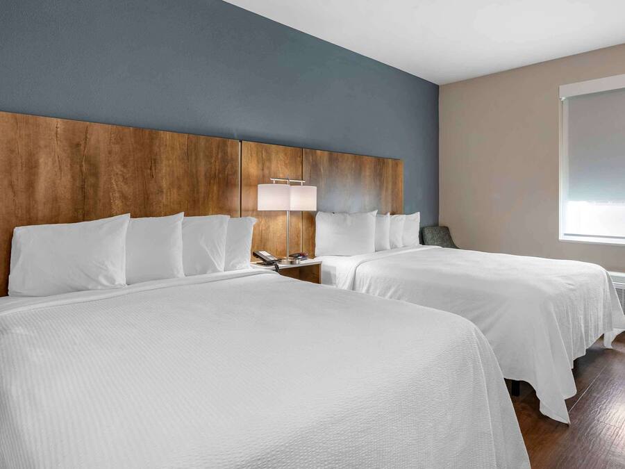 Una habitación de hotel con dos camas, cabecera de madera, lámpara de noche y un ventanal grande.