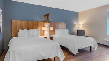 A hotel room with two beds, wooden headboards, bedside lamps, and a large window.