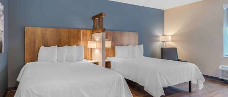 A hotel room with two beds, wooden headboards, bedside lamps, and a large window.