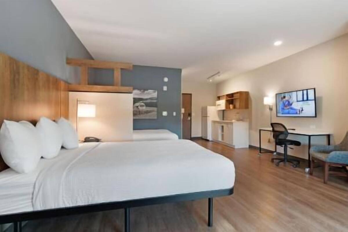Ein Hotelzimmer mit Bett, Schreibtisch, Stuhl, Fernseher und einer Küchenzeile.