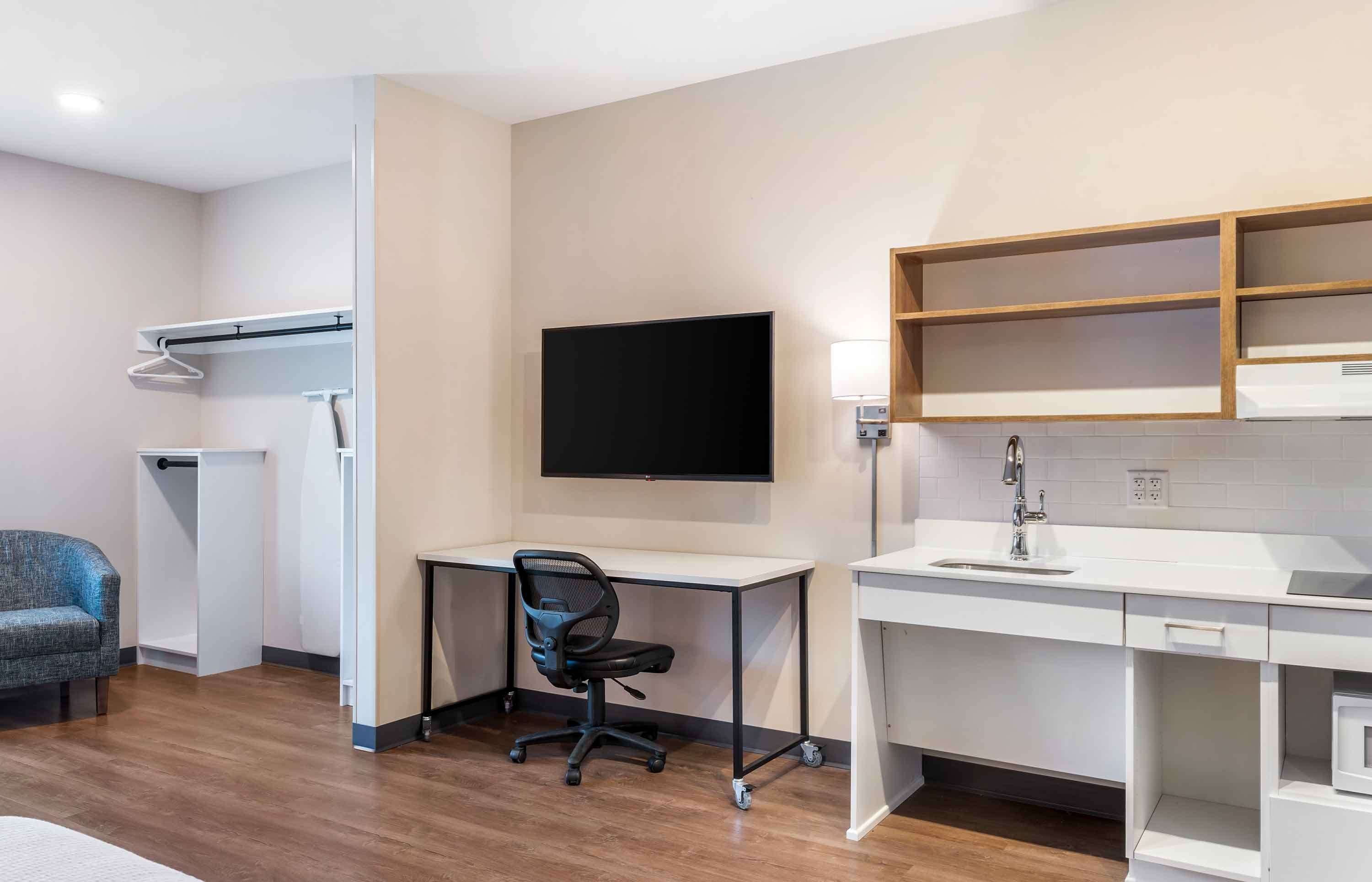 Habitación de hotel moderna con escritorio, silla, televisor y estanterías empotradas.