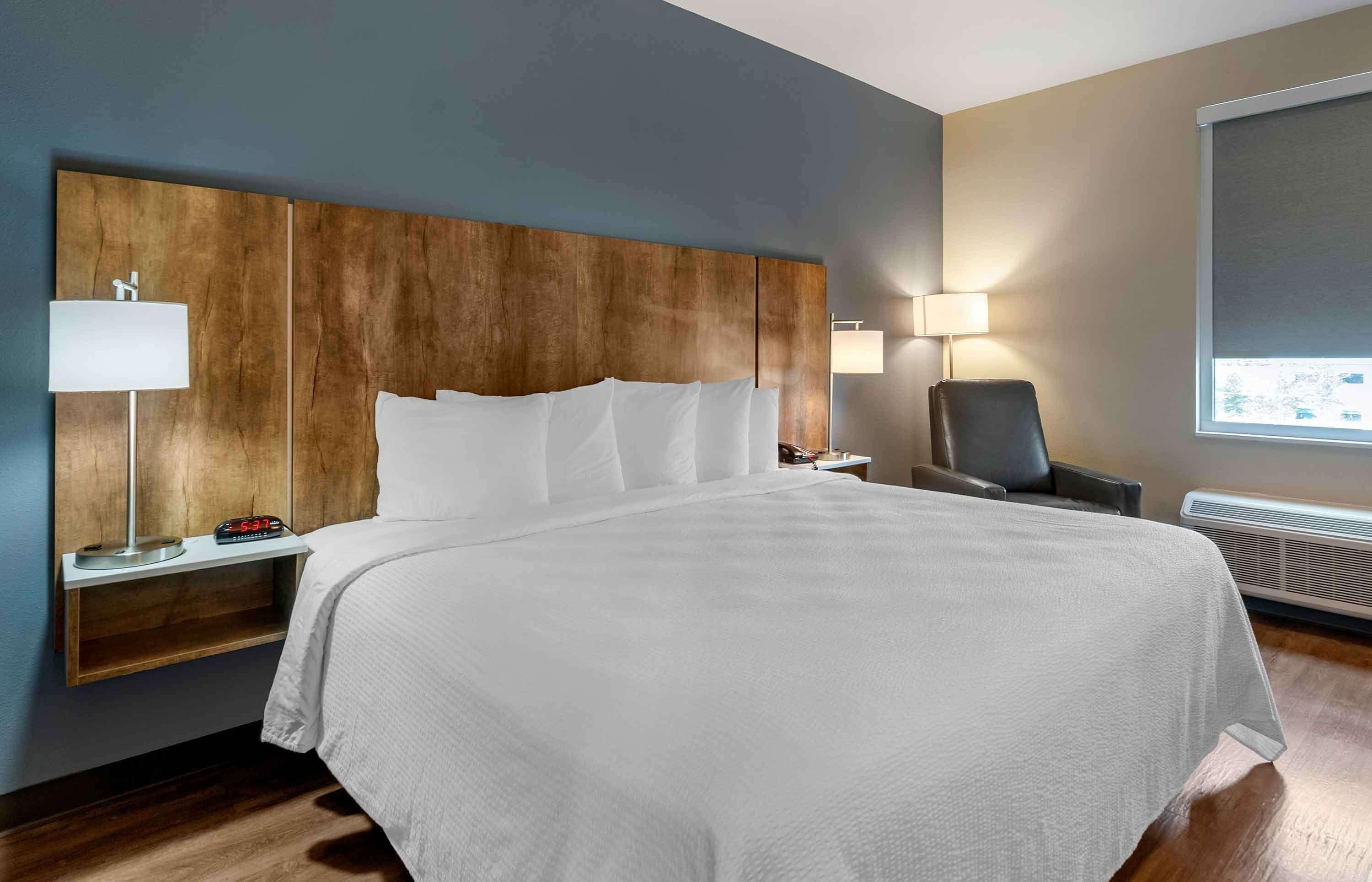 A hotel room with a large bed, two bedside tables with lamps, a chair, and a window with a view.