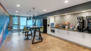 A modern kitchen area with a coffee station, dining table, and chairs.
