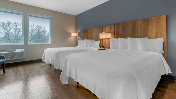 A hotel room with two beds, a large window with a view, a wooden headboard, and a floor heater.