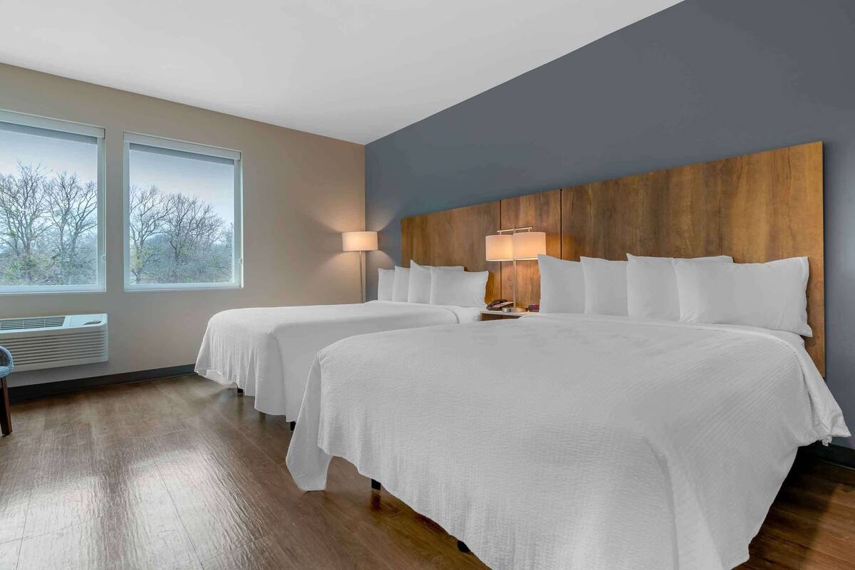 A hotel room with two beds, a large window with a view, a wooden headboard, and a floor heater.
