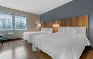 A hotel room with two beds, a large window with a view, a wooden headboard, and a floor heater.