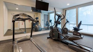 A gym with treadmills, elliptical machines, and a TV mounted on the wall.