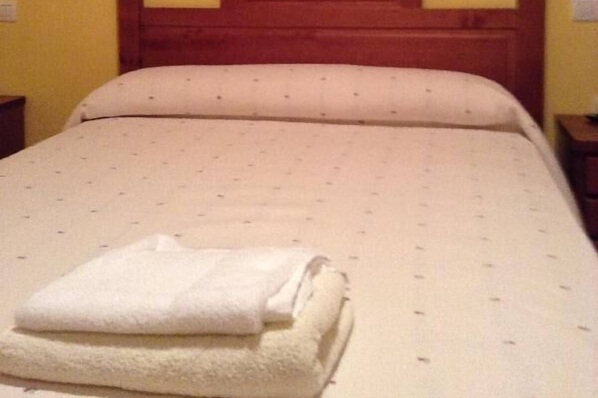 A bed with a wooden headboard, a white pillow, and a folded white towel on the bed.