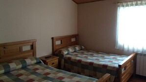 A room with two wooden beds, each with a checkered bedspread, a nightstand, and a window with curtains. - Casa Polín (Vega de Valcarce)