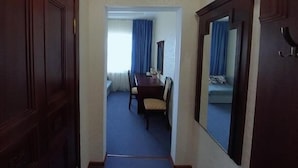 Un pasillo con alfombra azul que lleva a una habitación con una mesa de comedor, sillas, un espejo grande y un sofá.