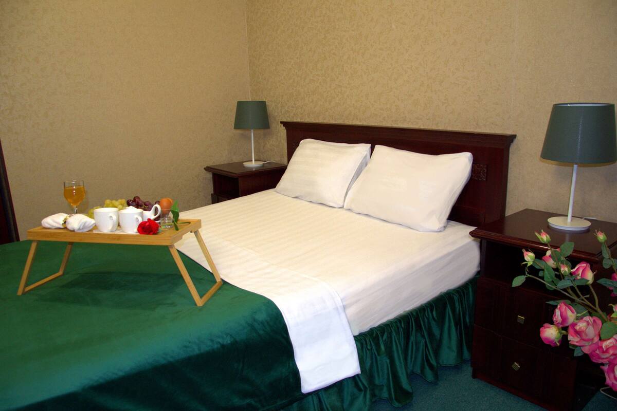 A neatly made bed with a green bedspread, a tray with breakfast items, and two bedside lamps.