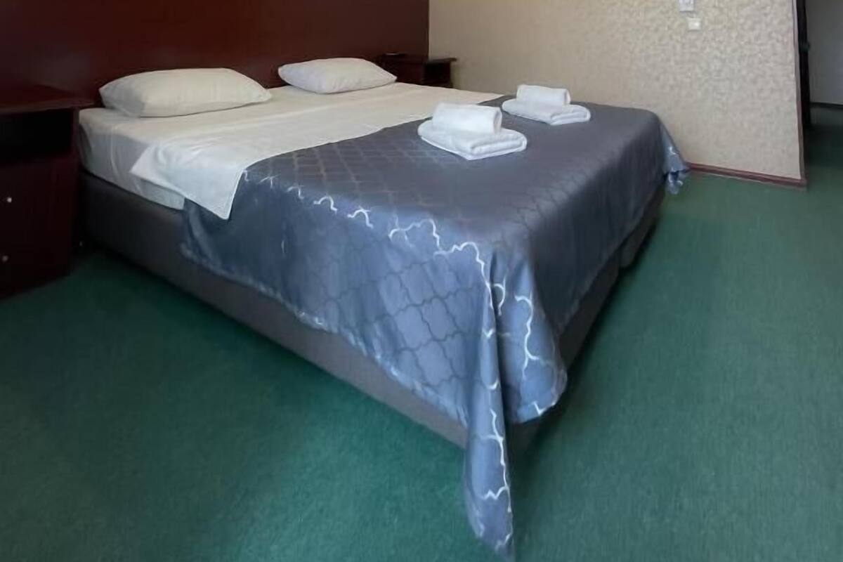 A hotel room with a large bed, two bedside tables, and a green carpet.