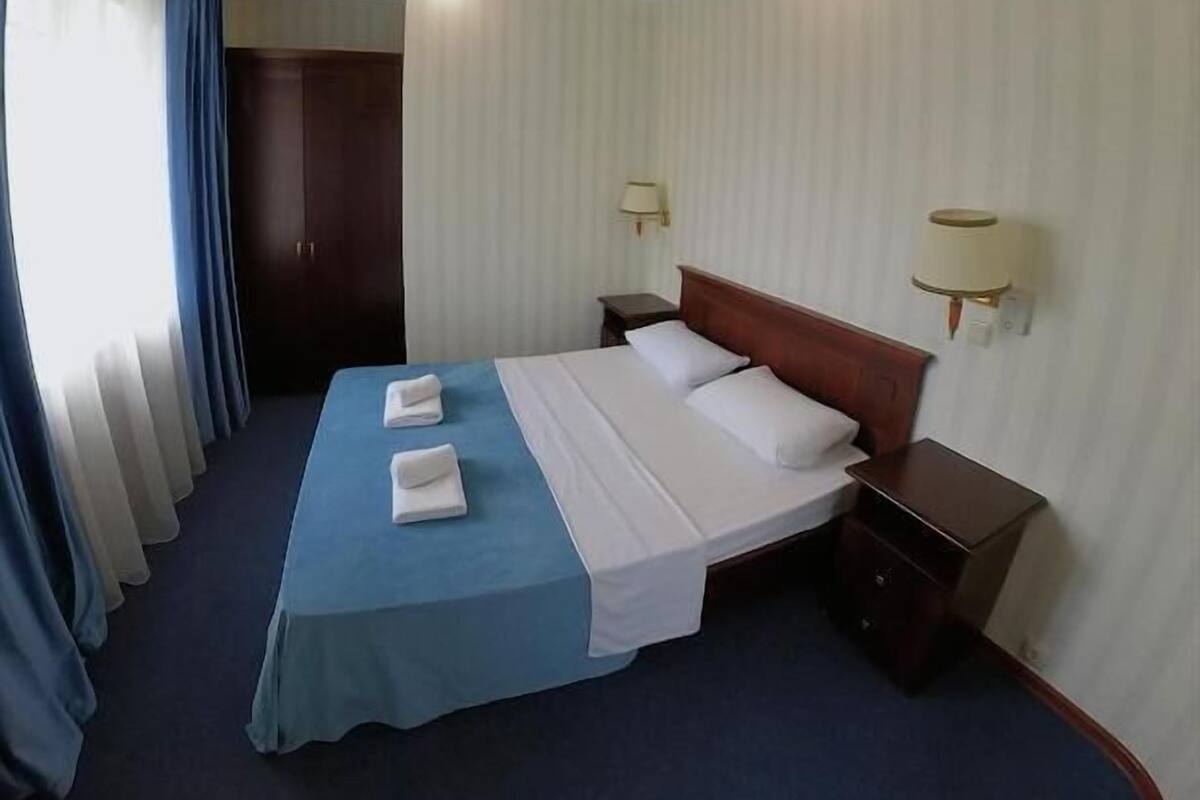A hotel room with a bed, two bedside tables, a wardrobe, and curtains.