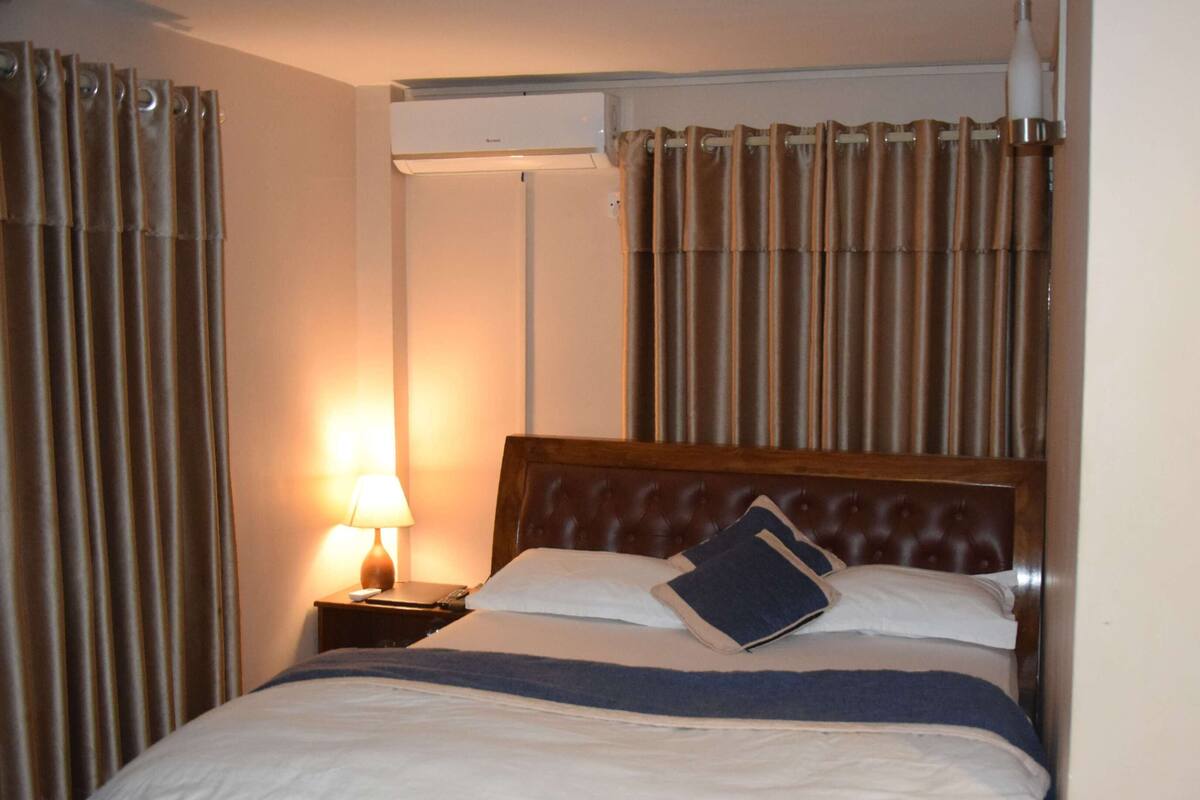 A hotel room with a bed, a nightstand, a lamp, and curtains.