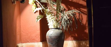 Eine große, dunkel gefärbte Vase mit floralem Muster auf Ablage neben einer roten Wand.