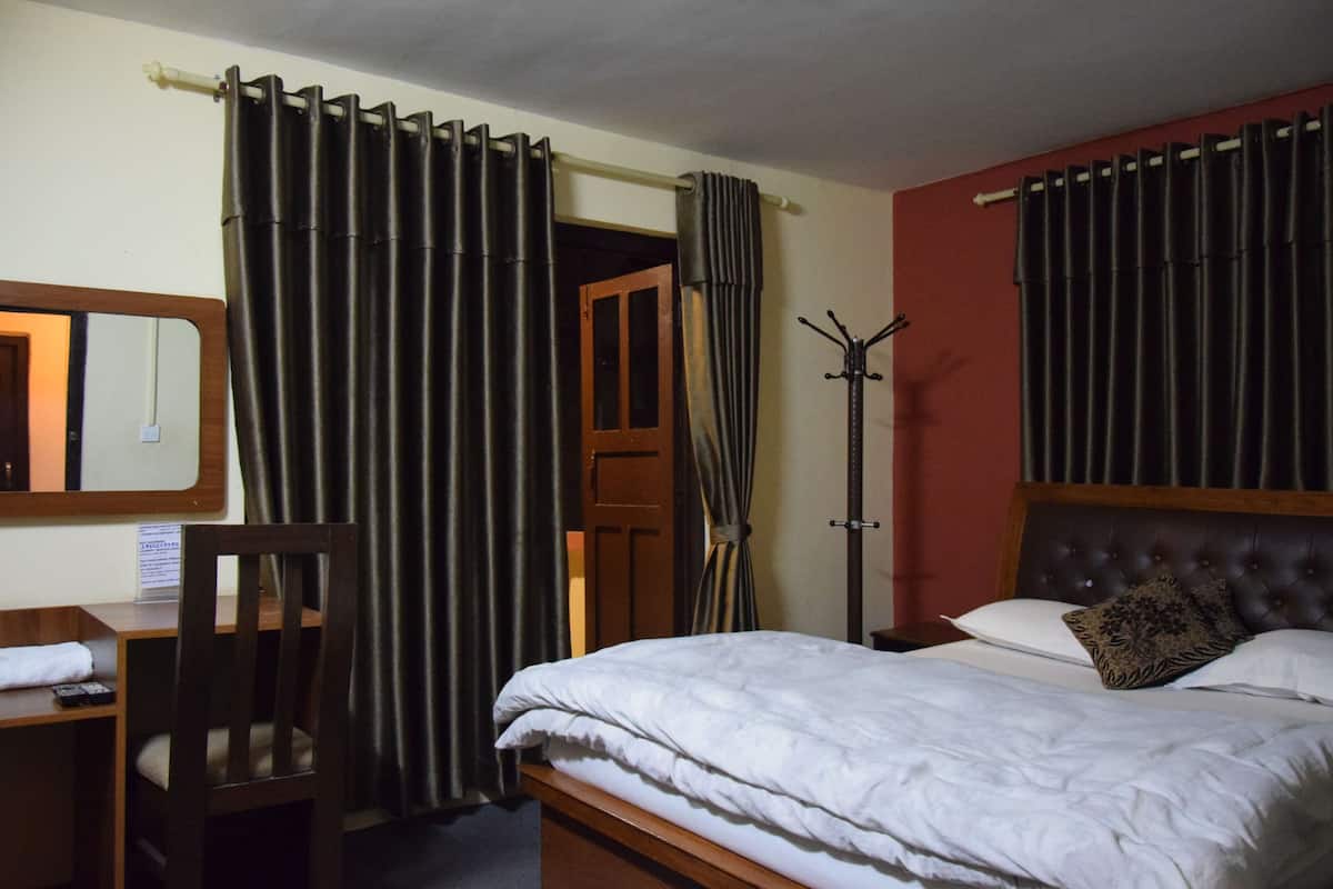 A hotel room with a bed, a desk, and a chair. There is a coat rack and a mirror on the wall.