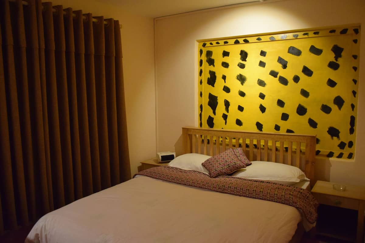 A hotel room with a bed, a nightstand, a lamp, and a large abstract painting on the wall.