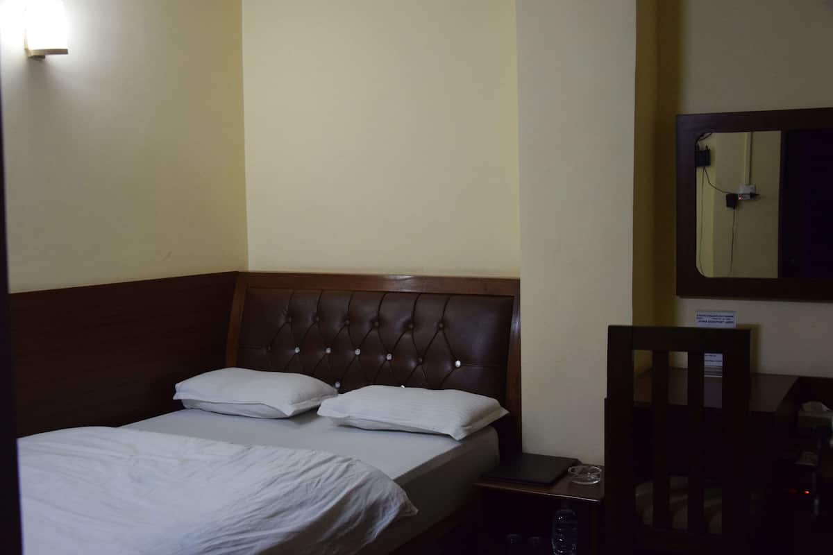 A hotel room with a single bed, a wooden headboard, a bedside table with a lamp, and a chair.