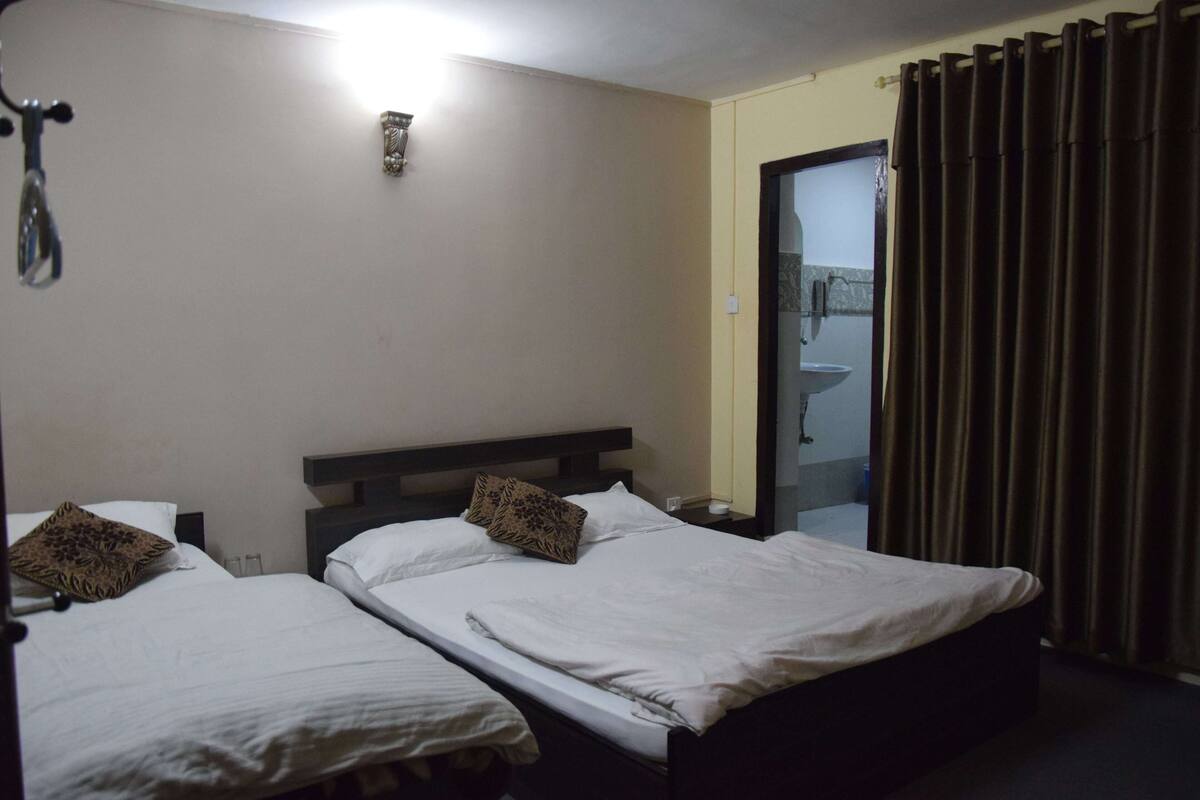 A hotel room with two single beds, a nightstand, a lamp, and a bathroom visible through an open door.