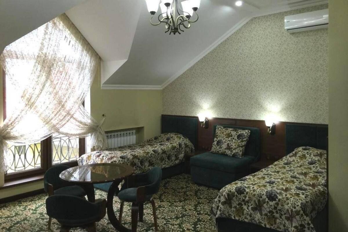 A room with two beds, a round table, and chairs, a chandelier, and a window with curtains.