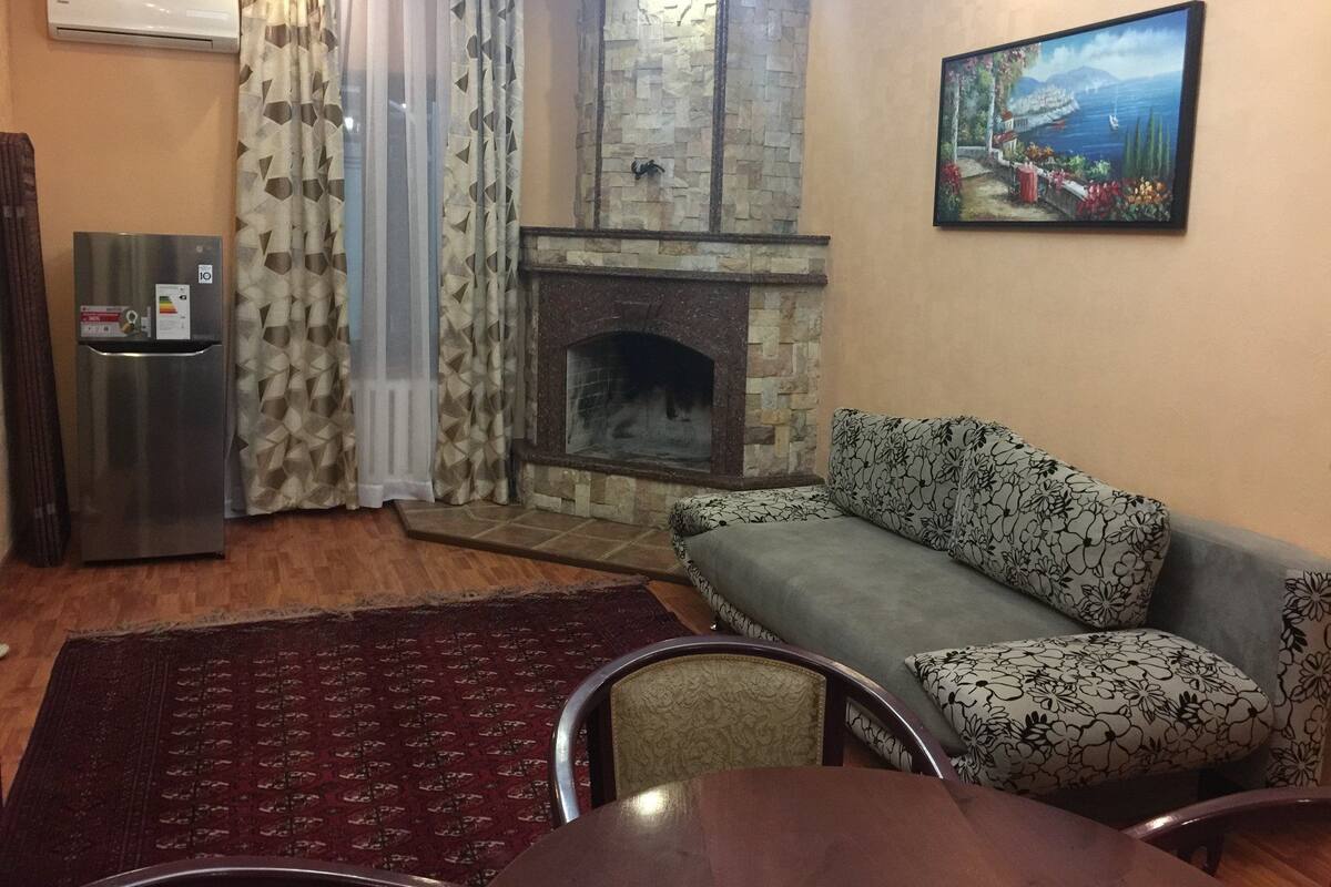 A living room with a stone fireplace, a sofa, a dining table, and a painting on the wall.