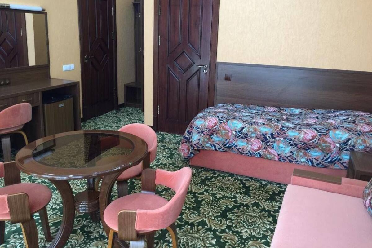 A hotel room with a bed, a round table with chairs, a dresser, and two doors.
