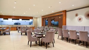 A spacious dining area with multiple tables and chairs, a kitchen in the background, and decorative wall art.