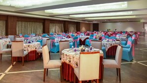 A banquet hall with multiple round tables, each with floral tablecloths and blue chairs.