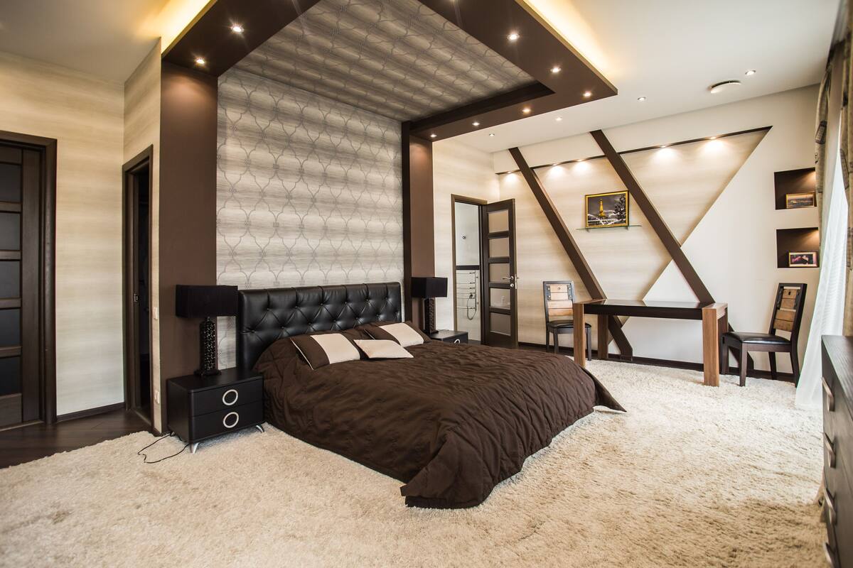 Un dormitorio moderno con una cama grande, un escritorio y una silla. Hay un televisor sobre un mueble bajo y una estantería.