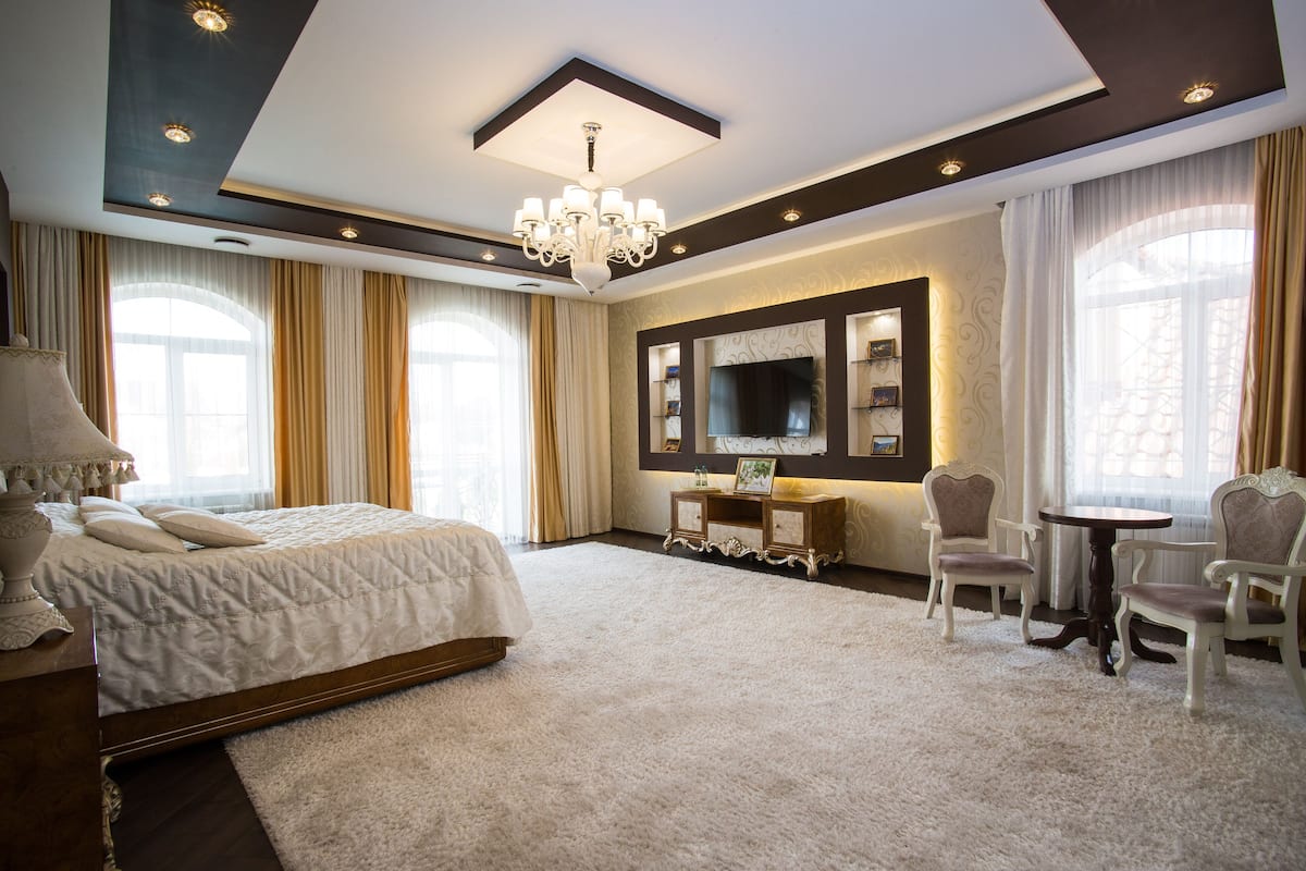 Un dormitorio amplio con una cama grande, un candelabro, un televisor y una zona de estar con dos sillones.