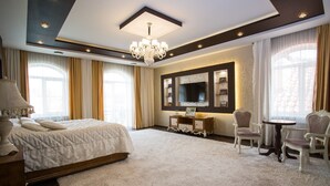Un dormitorio amplio con una cama grande, un candelabro, un televisor y una zona de estar con dos sillones.