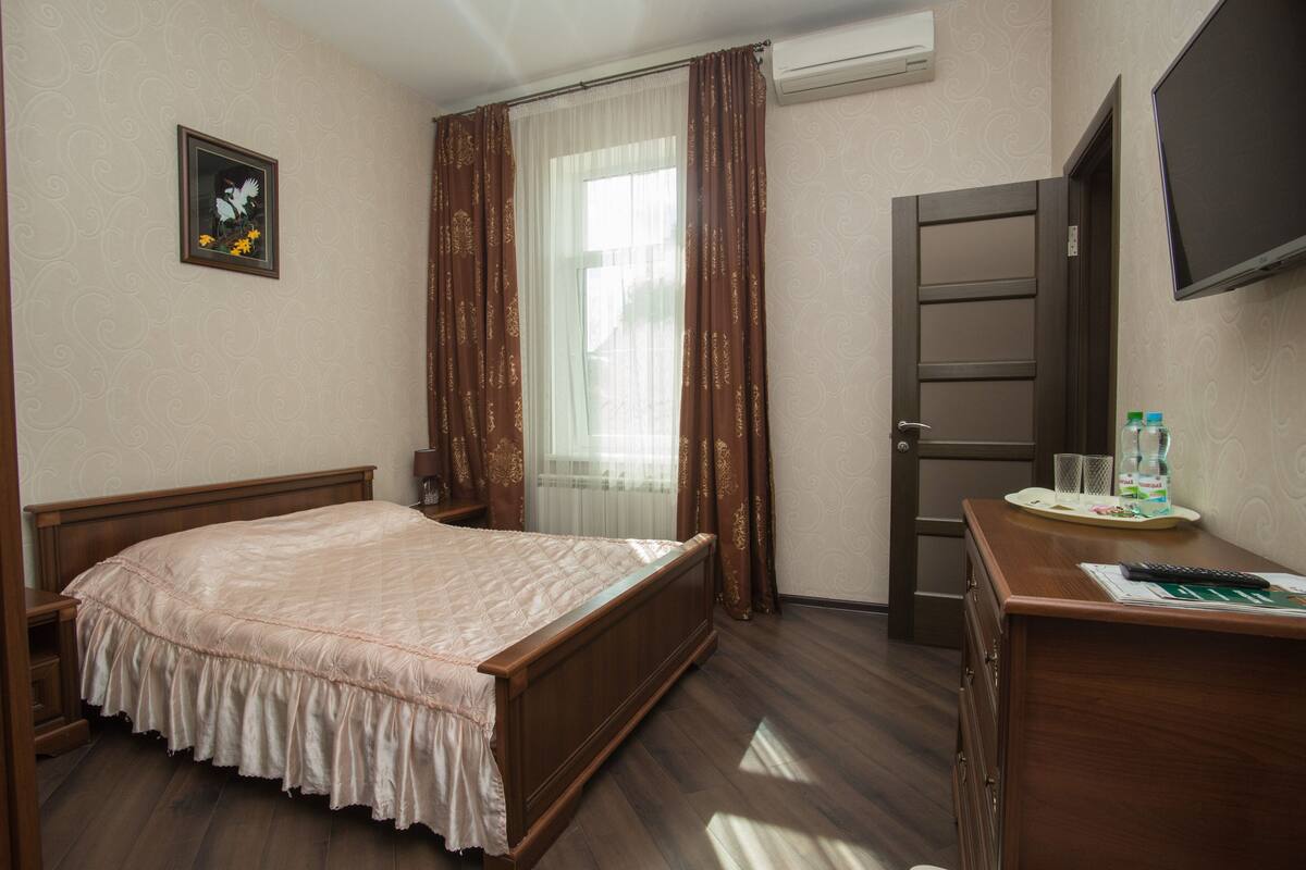 Una habitación de hotel con cama, escritorio con espejo, televisor y ventana con cortinas.