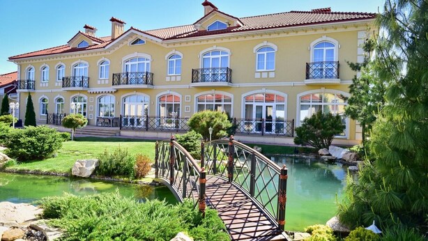Un edificio grande y amarillo con varios balcones y un estanque al frente.