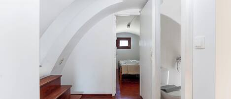 A narrow hallway with wooden stairs leading to a bedroom with a bed and a window.