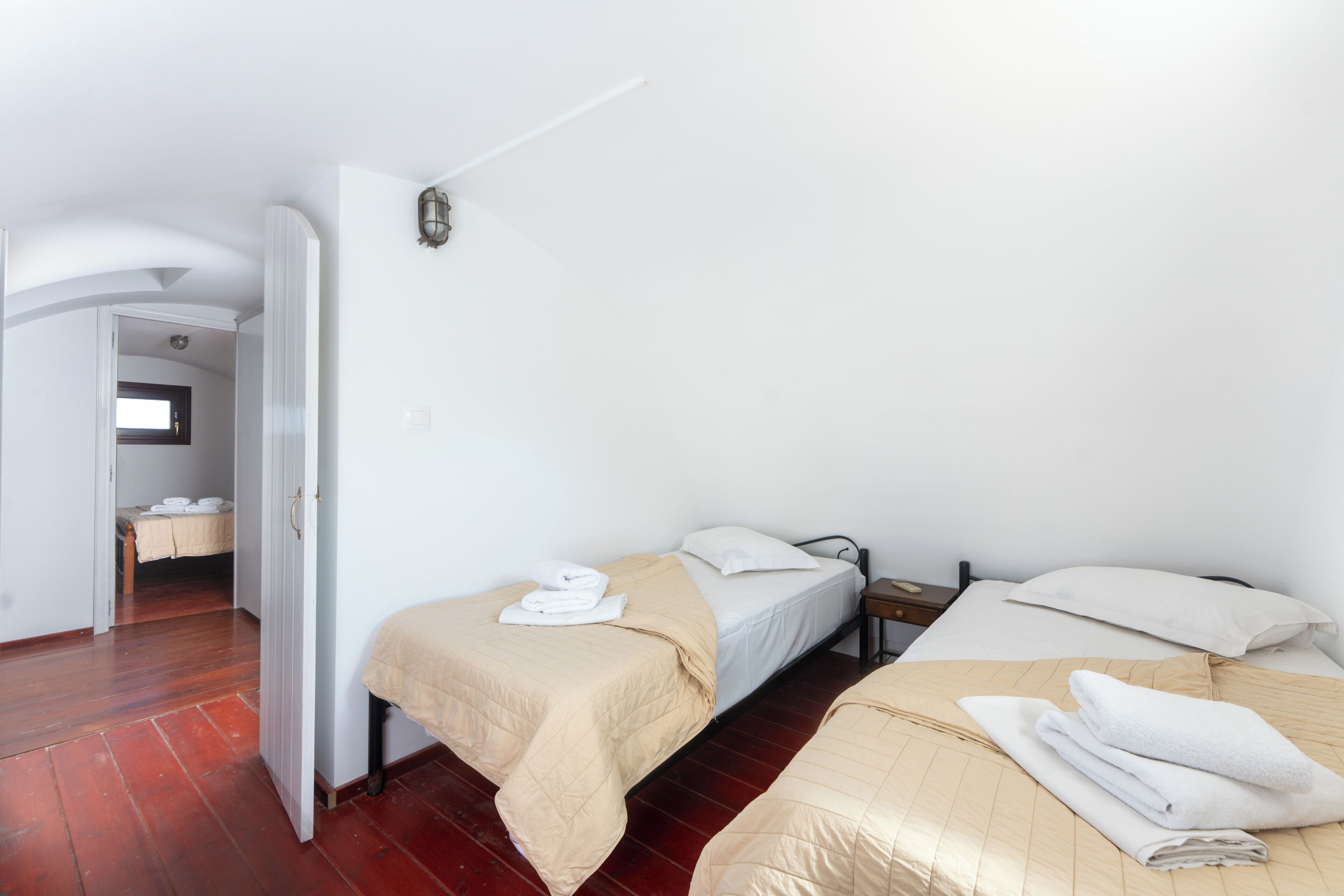 Ein Zimmer mit zwei Betten, Holzboden, weißer Wand und einer Tür zu einem anderen Raum.