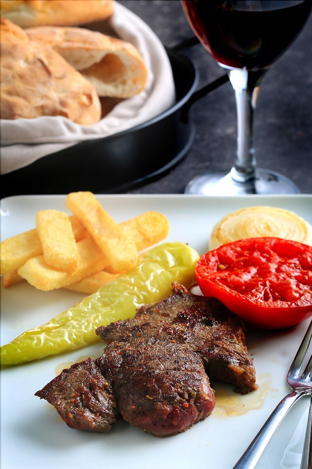A plate with grilled steak, French fries, a slice of tomato, and a green chili pepper.